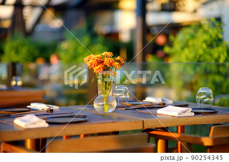 Outdoor cafe on sunny summer day. Stylish table decoration with natural flowers bouquet. Outdoor cafe on sunny summer day. Stylish table decoration with natural flowers bouquet. 90254345