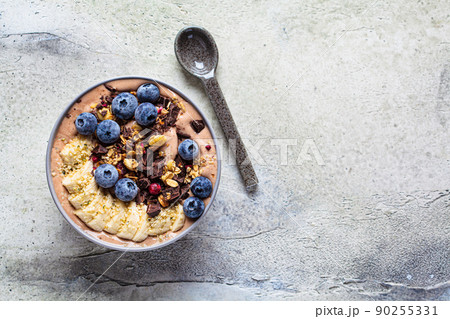 Chocolate banana smoothie bowl with granola, berries and hemp seeds, gray background. Healthy vegan recipe concept. Chocolate banana smoothie bowl with granola, berries and hemp seeds, gray background. Healthy vegan recipe concept. 90255331