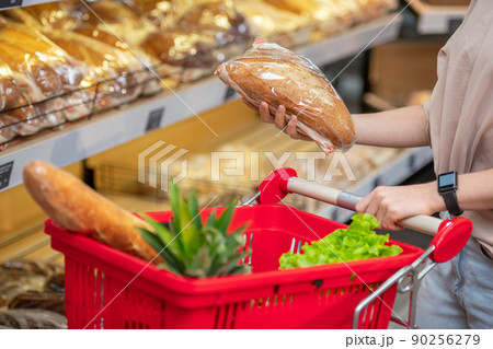 Modern young woman with long hair choosing bread in grocery store in morning, copy space 90256279