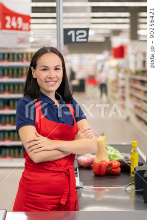 Cheerful woman working in supermarket sitting at cash desk looking at camera smiling 90256421