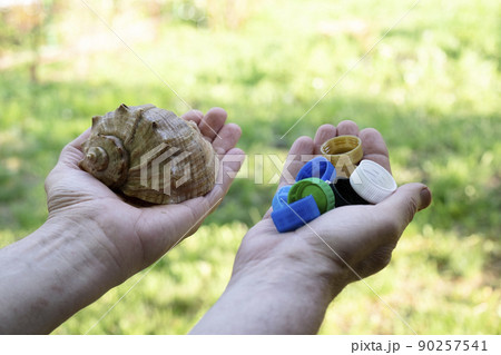 Hands hold a beautiful sea shell and many plastic bottle caps. The concept of choosing wildlife or plastic. Environmental pollution 90257541