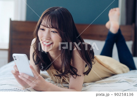 ベッドでスマホを操作する若い女性のライフスタイルイメージ 90258136