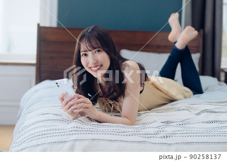 ベッドでスマホを操作する若い女性のライフスタイルイメージ 90258137