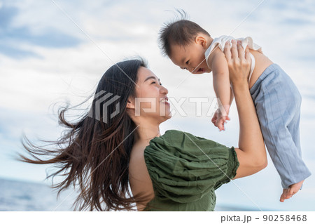 Happy Joyful mother and Son having fun Playing on the Beach together. Asian mom walks by ocean on the beach and throwing up her son in the air at the tropical view. Motherhood Family Concept. Happy Joyful mother and Son having fun Playing on the Beach together. Asian mom walks by ocean on the beach and throwing up her son in the air at the tropical view. Motherhood Family Concept. 90258468