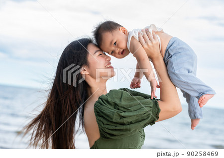 Happy Joyful mother and Son having fun Playing on the Beach together. Asian mom walks by ocean on the beach and throwing up her son in the air at the tropical view. Motherhood Family Concept. 90258469