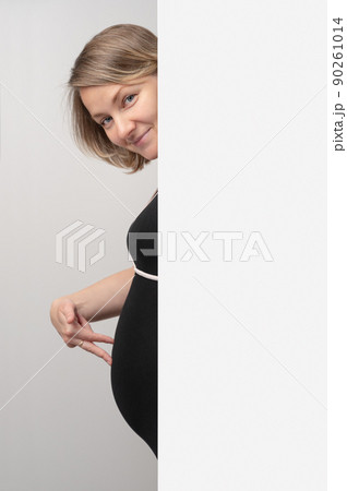 Pregnant woman peeking out of white wall. Happy Pregnant Woman touching belly with hand fingers. Baby expectation. Playing on baby bump. Pregnant woman peeking out of white wall. Happy Pregnant Woman touching belly with hand fingers. Baby expectation. Playing on baby bump. 90261014