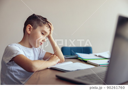 Portrait of sad tired and lazy small boy having online video lesson at laptop. At home. 90261760