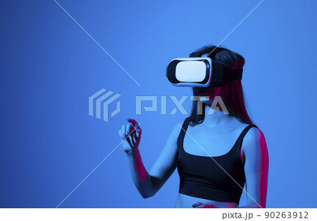 Portrait of young woman playing in VR-glasses in neon light on blue background. Concept modern gadgets and technologies. Future technology concept. Virtual reality gaming. 90263912