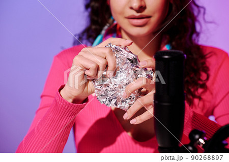 Selective focus of young woman creating content for ASMR blog squeezing foil in front of microphone 90268897
