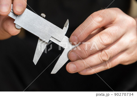 A man's hand holding a caliper. An adult man with a high-precision metal instrument for measuring the external and internal dimensions of objects and the depths A man's hand holding a caliper. An adult man with a high-precision metal instrument for measuring the external and internal dimensions of objects and the depths 90270734