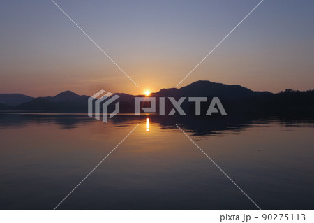 海の日の出シーン　静かな海面と湾を取り巻く低い山々　そこから顔を出した朝陽 90275113