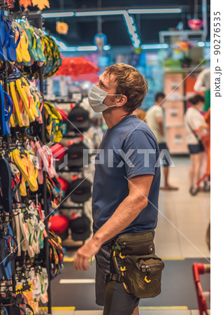 Serious man blue in blue t-shirt choosing shoes in store, wearing blue face mask protect from virus COVID, public personal health control measure, shopping during pandemic, buying new clothing 90276535