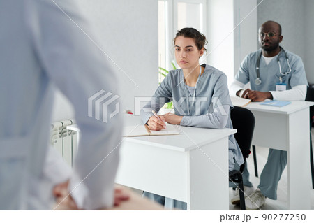 Medical students in uniform sitting at desks learning how to provide first aid during training 90277250