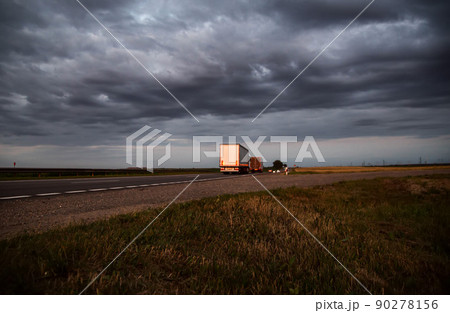 A column of trucks with trailers carry cargo in the evening against a cloudy sky with clouds. Direct FTL transportation model. Copy space for text, expedited shipping 90278156