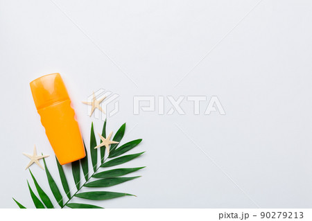 Sunscreen spray bottle. Bottle with sun protection cream and sea shells with tropical green leaf on color background, top view 90279213