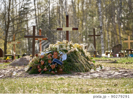 New grave with wooden cross and several funeral wreaths. Another graves with crosses behind it. Forest at the background. New grave with wooden cross and several funeral wreaths. Another graves with crosses behind it. Forest at the background. 90279291