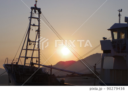 隠岐島西郷港の日の出　小型貨物船のクレーンの先に昇オレンジ色の朝陽　ダイナミックな夜明けの光景 90279436