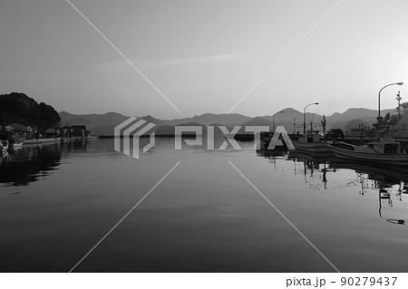 モノクローム夜明けの風景　静かな海面に映る小型漁船の影　目の前に広がる鏡面の様な海とモヤのかかる山 90279437