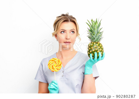 Young caucasian female doctor nutritionist holding fresh pineapple with lollipop over white background 90280287