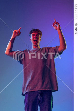 Young red-headed man, student isolated over blue studio background in neon light. Concept of youth, fashion, emotions, facial expression 90286459