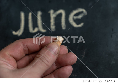 Adult male holding a piece of yellow chalk in his hand. Handwritten word JUNE on black chalkboard. Selective focus. 90286543