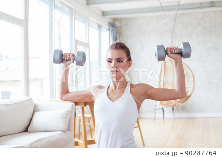 Athletic woman in sportswear doing fitness exercises with dumbbells at home. Athletic woman in sportswear doing fitness exercises with dumbbells at home. 90287764