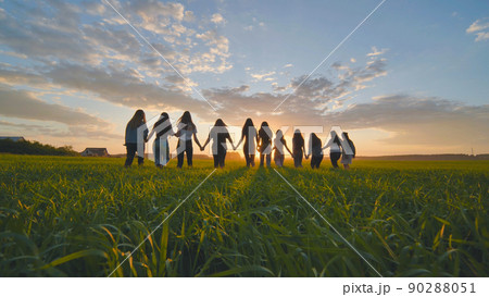 A group of girls walk towards the sun at sunset holding hands. A group of girls walk towards the sun at sunset holding hands. 90288051