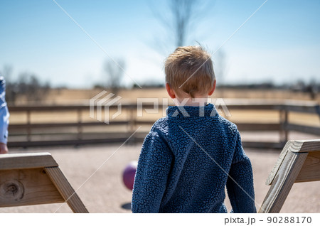 Child waiting along fence for next round of gaga ball in a school playground. Child waiting along fence for next round of gaga ball in a school playground. 90288170
