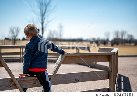 Child waiting along fence for next round of gaga ball in a school playground. Child waiting along fence for next round of gaga ball in a school playground. 90288183
