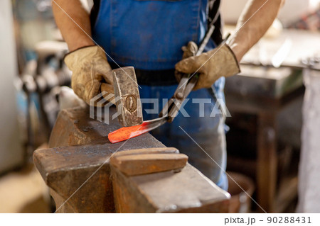 Close up view of heated metal and anvil. The blacksmith in the production process of metal products handmade in the forge. Blacksmith forging metal with a hammer. Metal industry, old profession. Close up view of heated metal and anvil. The blacksmith in the production process of metal products handmade in the forge. Blacksmith forging metal with a hammer. Metal industry, old profession. 90288431