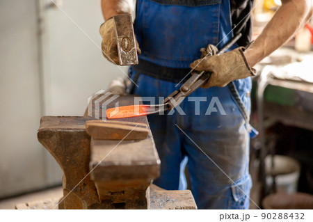Close up view of heated metal and anvil. The blacksmith in the production process of metal products handmade in the forge. Blacksmith forging metal with a hammer. Metal industry, old profession. 90288432