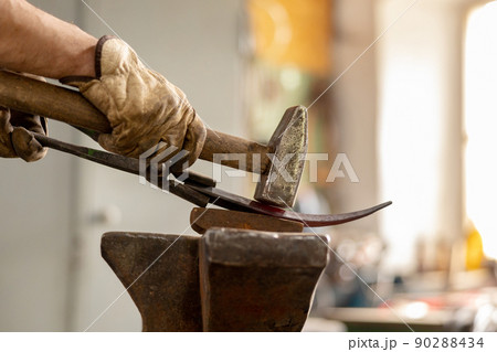 Close up view of heated metal and anvil. The blacksmith in the production process of metal products handmade in the forge. Blacksmith forging metal with a hammer. Metal industry, old profession. Close up view of heated metal and anvil. The blacksmith in the production process of metal products handmade in the forge. Blacksmith forging metal with a hammer. Metal industry, old profession. 90288434