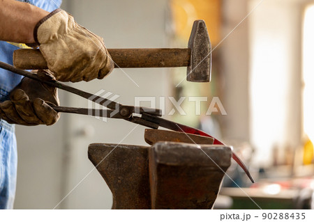 Close up view of heated metal and anvil. The blacksmith in the production process of metal products handmade in the forge. Blacksmith forging metal with a hammer. Metal industry, old profession. Close up view of heated metal and anvil. The blacksmith in the production process of metal products handmade in the forge. Blacksmith forging metal with a hammer. Metal industry, old profession. 90288435