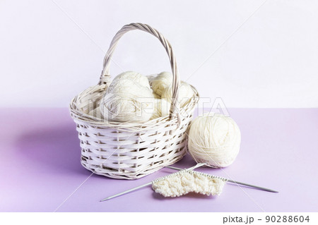 White balls of thread in a basket on a lilac background for knitting warm clothes and hobbies needlework 90288604