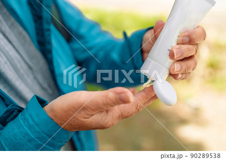 Caucasian woman hands applying sunscreen lotion from a white tube while traveling in the mountains 90289538