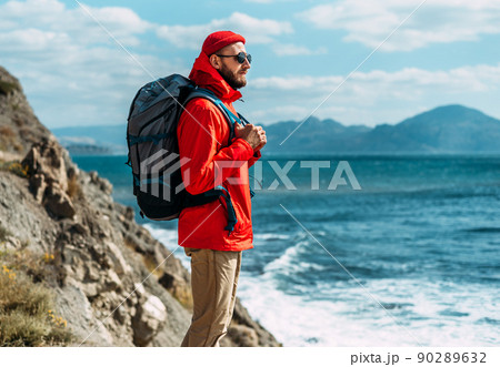 A tourist with a backpack on his back stands against the backdrop of a beautiful seascape. A traveler with his tourist backpack stands against the background of the sea. Copy space A tourist with a backpack on his back stands against the backdrop of a beautiful seascape. A traveler with his tourist backpack stands against the background of the sea. Copy space 90289632