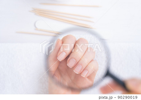 We examine the nails on the female hand through a magnifying glass. Attention to the condition of nails and skin. Nearby are manicure items, orange tree sticks and a nail file 90290019