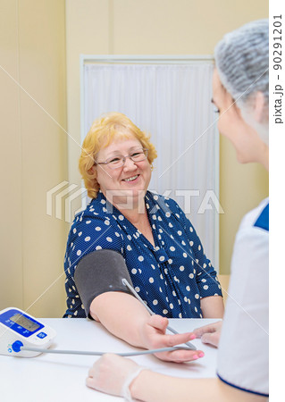 A nurse in a polyclinic measures the blood pressure of a woman with a device. Healthcare 90291201