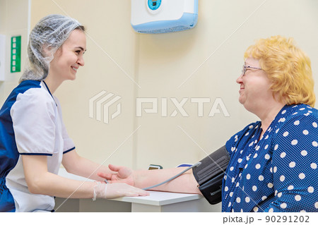A nurse in a polyclinic measures the blood pressure of a woman with a device. Healthcare 90291202