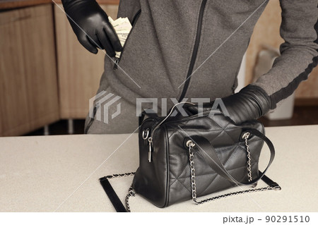 Robber in black outfit and gloves see in opened stolen women bag. The thief takes out the gold and money from a womans handbag in kitchen 90291510