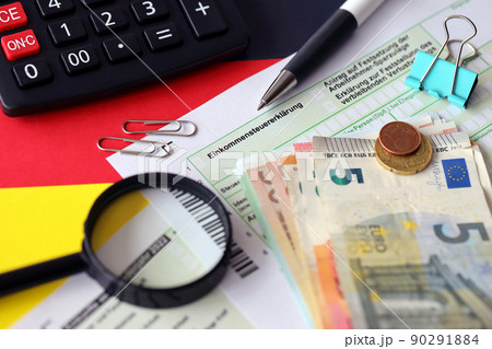 German income tax return form with pen and european euro money bills lies on flag close up. Taxpayers in Germany using euro currency to pay taxes 90291884