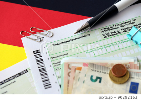 German income tax return form with pen and european euro money bills lies on flag close up. Taxpayers in Germany using euro currency to pay taxes 90292163