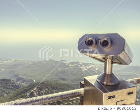 binoculars on an observation deck made of gray metal. sightseeing tour, observing the view from the mountains. binoculars against the backdrop of a mountainous plain with greenery 90301015