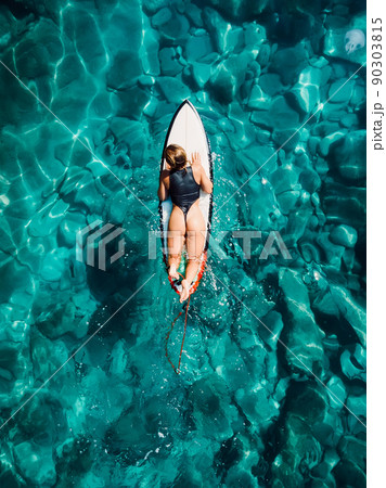 Pretty surfer woman floating on surfboard in tropical ocean. Aerial view Pretty surfer woman floating on surfboard in tropical ocean. Aerial view 90303815