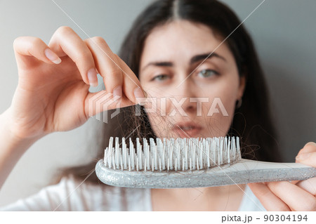 Young woman pulls out a clump of hair from a comb in bewilderment. Close-up. The concept of alopecia and hair loss Young woman pulls out a clump of hair from a comb in bewilderment. Close-up. The concept of alopecia and hair loss 90304194