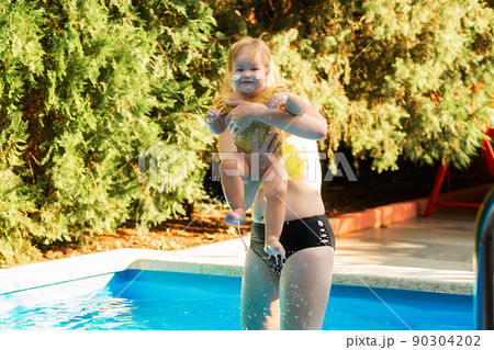 A mother plays with her little daughter in the pool. Summertime 90304202