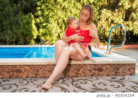 A young Caucasian mother wipes her little daughter sitting by the pool. Happy childhood and summer A young Caucasian mother wipes her little daughter sitting by the pool. Happy childhood and summer 90304204