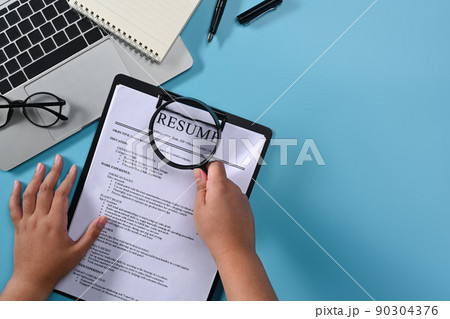 Above view woman holding a magnifying glass over resumes of applicants. Job search concept 90304376