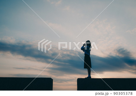 制服姿の女子高生のシルエットと美しい夕焼け空 90305378