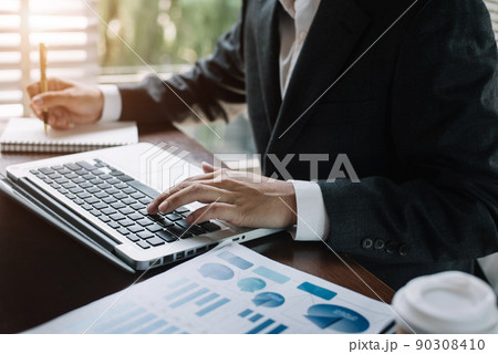 Businessman hands typing on computer keyboard and take notes  calculate and analyzing graph document financial in office. 90308410